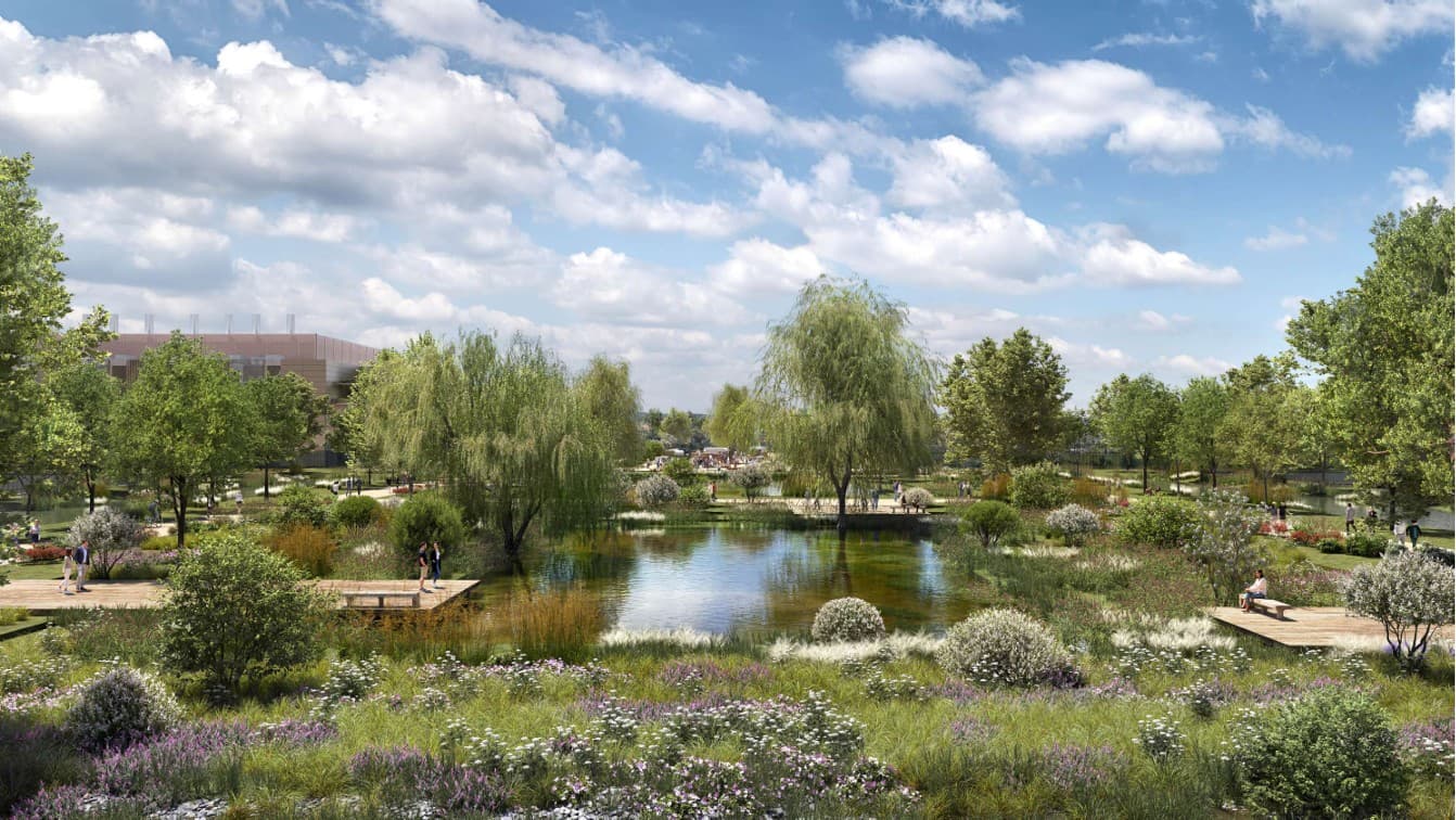 Vue du parc central aménagé autour d'un bassin, avec saules pleureurs, prairies fleuries et personnes circulant sur les cheminements en bois.