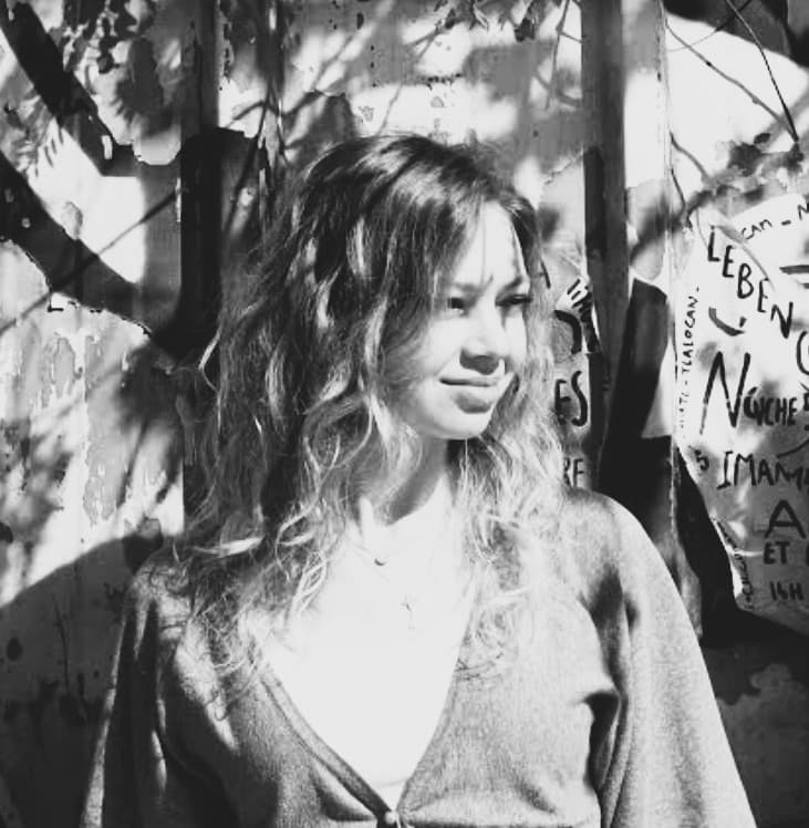 Portrait en noir et blanc d'Aleksandra Zawartka en extérieur, à contre-jour sous des branches d'arbre.