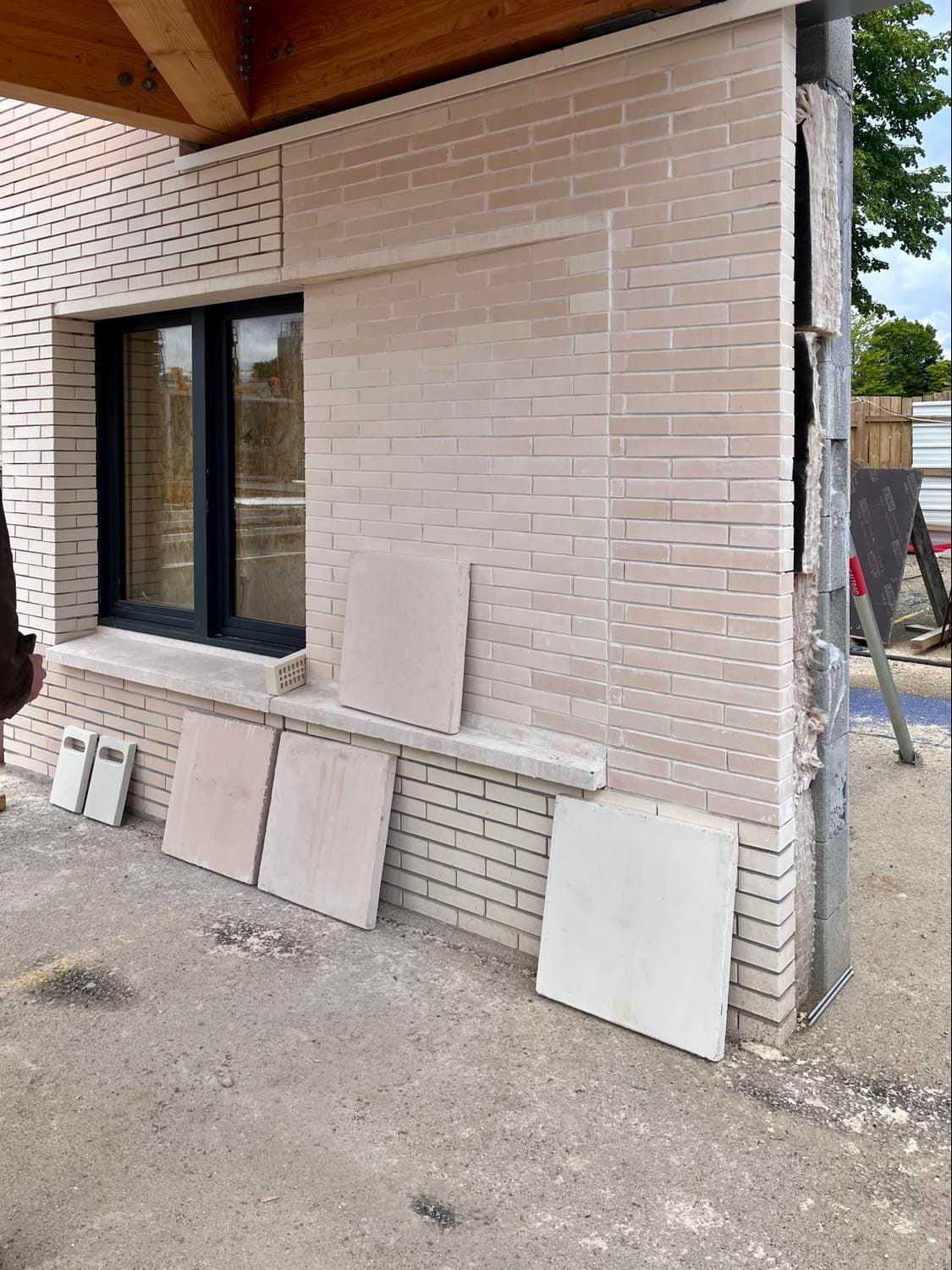 Photo de chantier d'un panneau prototype de façade en briques claires, avec échantillons de teintes posés au pied du mur.
