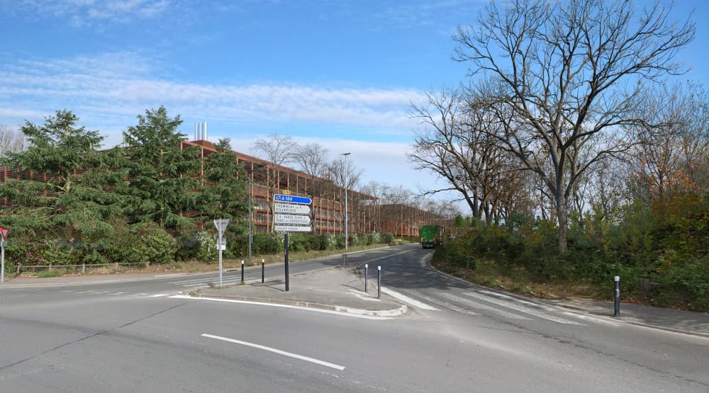 Vue hivernale depuis la voie d'accès au site, avec le bâtiment du data center en arrière-plan, arbres dénudés et poids lourd circulant sur la voie.